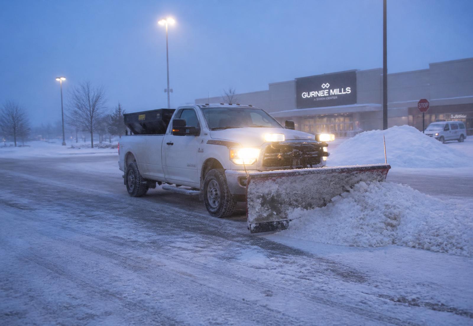 Snow plow truck clearing a commercial parking lot during a Michigan winter storm